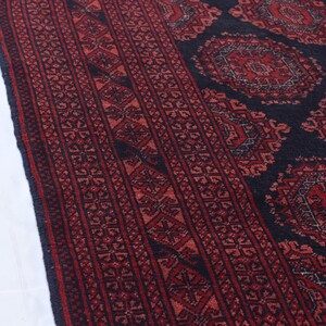May include: A close-up of a red and black patterned rug with intricate designs. The rug has a traditional Persian style with a central medallion and repeating border patterns.
