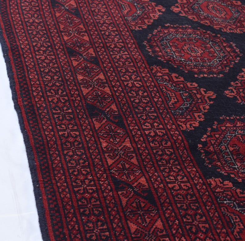 May include: A close-up of a red and black patterned rug with intricate designs. The rug has a traditional Persian style with a central medallion and repeating border patterns.