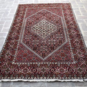 May include: A traditional Persian rug with a red, white and black colour scheme. The rug features a central medallion with intricate floral and geometric patterns. The rug has a fringed border.