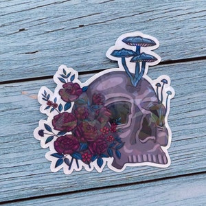 May include: A sticker featuring a purple skull with a bouquet of dark pink roses and blue mushrooms growing from the top of the skull.