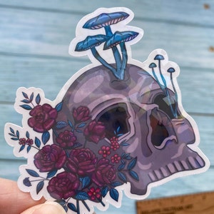 May include: A sticker featuring a purple and blue skull with a cluster of blue mushrooms growing from the top. The skull is surrounded by a bouquet of dark red roses and small pink flowers.