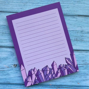 May include: Purple lined notepad with a border of purple and pink crystals at the bottom.