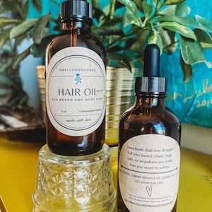 Könnte beinhalten: Zwei bernsteinfarbene Glasflaschen mit Tropfern, eine mit der Aufschrift "HAIR OIL" für Bart und Körperhaare, die andere mit Gebrauchsanweisung und Inhaltsstoffen. Beide Flaschen haben braune Papieretiketten mit weißem Text.