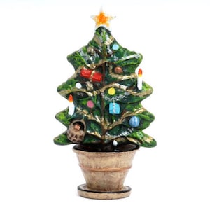 Puede incluir: Un pequeño árbol de Navidad verde con una estrella dorada en la cima, decorado con adornos y velas de colores. El árbol está en una maceta marrón con un borde dorado.