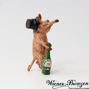 Peut inclure: Une petite figurine en bronze d'un cochon portant un chapeau haut de forme et tenant une bouteille de champagne verte. La bouteille porte l'inscription "CHAMPAGNE" et "GRAND CRU".