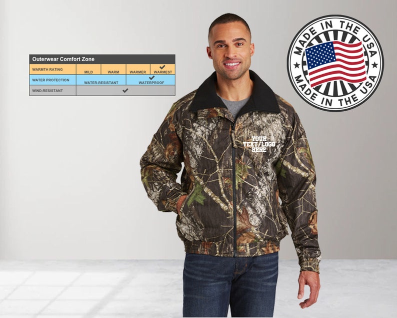 May include: A camouflage print jacket with a black fleece lining. The jacket has a zipper closure and two pockets. The jacket is water-resistant and wind-resistant. The jacket is made in the USA. The text "YOUR TEXT/LOGO HERE" is embroidered on the jacket.