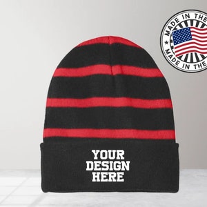 May include: Black and red striped knit beanie with a black cuff. The cuff has the text "YOUR DESIGN HERE" in white.