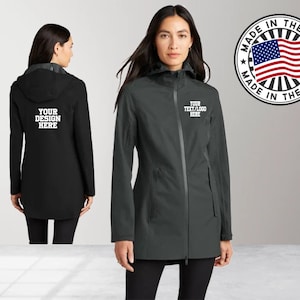 May include: A dark gray hooded jacket with a zipper closure. The jacket has two pockets on the front and a drawstring hood. The jacket is made in the USA. The text "YOUR TEXT/LOGO HERE" is embroidered on the front of the jacket.