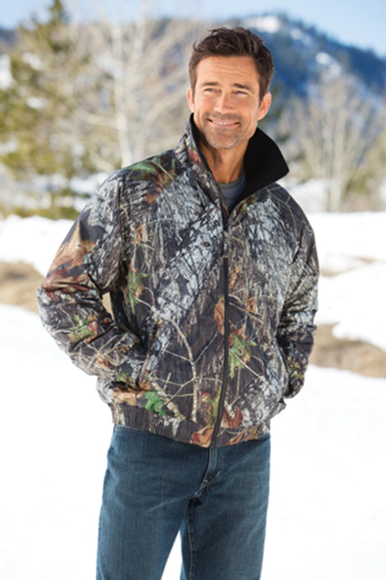 May include: A camouflage print jacket with a black zipper and a black fleece lining. The jacket has a stand-up collar and two pockets.