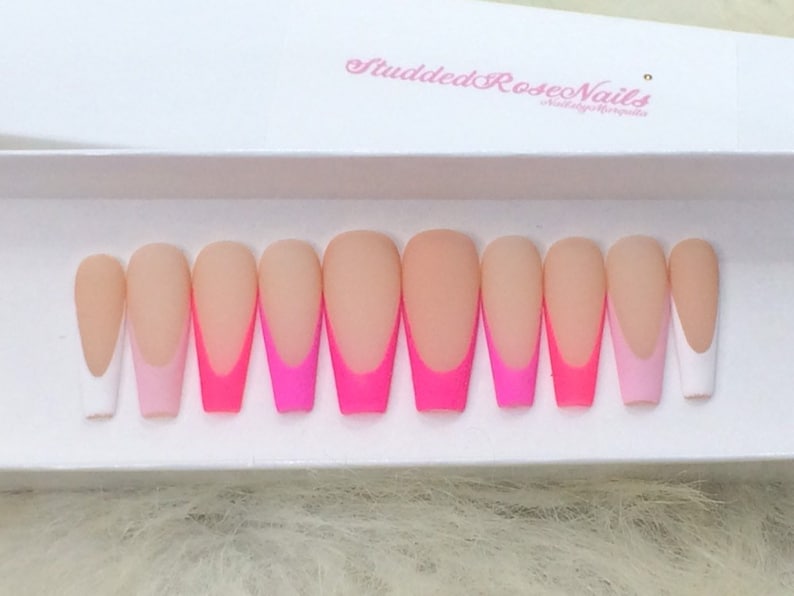 May include: Set of ten long, almond-shaped false nails with a white tip and a pink and neon pink ombre design. The nails are arranged in a row on a white surface.