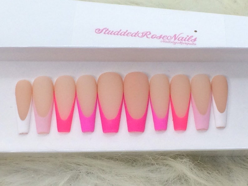 May include: Set of ten long, almond-shaped false nails with a white tip and a pink and hot pink ombre design. The nails are arranged in a row on a white surface. "Studded Rose Nails" is written on the surface.
