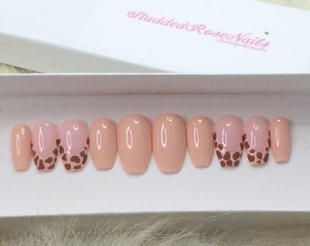 Puede incluir: Un conjunto de diez uñas postizas de color nude en forma de ataúd con un diseño de estampado de leopardo marrón en las puntas.