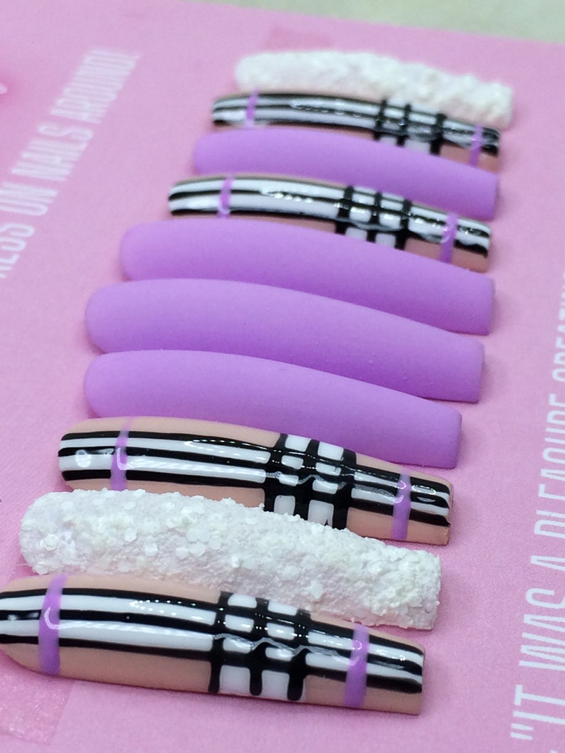 May include: Set of long, lavender and pink press-on nails with a black and white plaid design and white glitter accents.