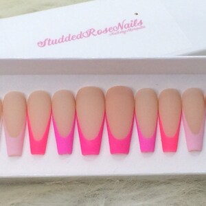 May include: Set of ten long, almond-shaped, fake nails with a white tip and a pink and hot pink ombre design. The nails are in a white box with the text "StuddedRoseNails" in pink.