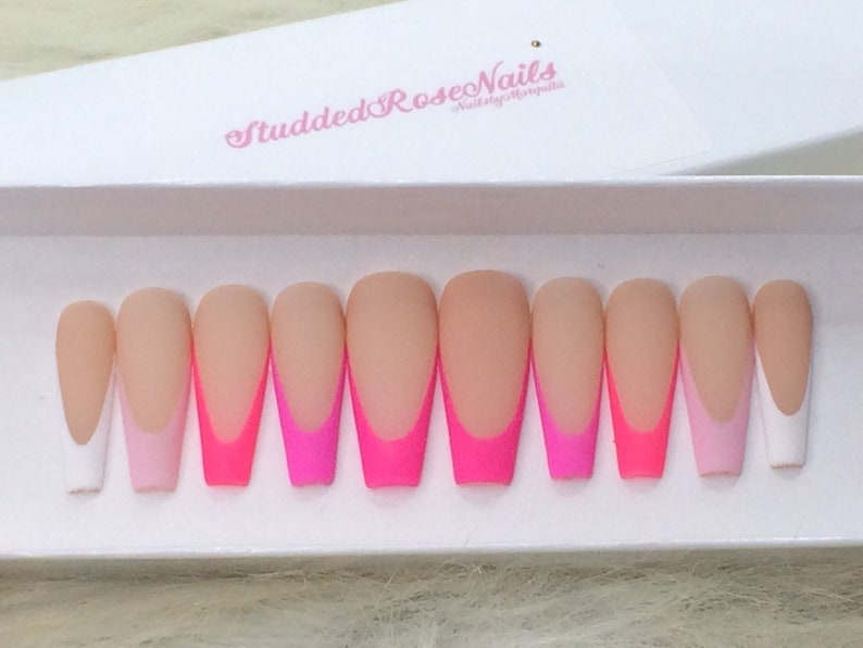 May include: Set of ten long, almond-shaped, fake nails with a white tip and a pink and hot pink ombre design. The nails are in a white box with the text "StuddedRoseNails" in pink.