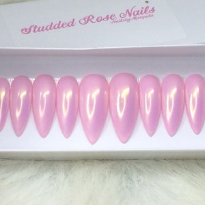 May include: A set of ten pink stiletto false nails with a pearlescent finish. The nails are in a white box with the text "Studded Rose Nails" and "Nails by Marquita".