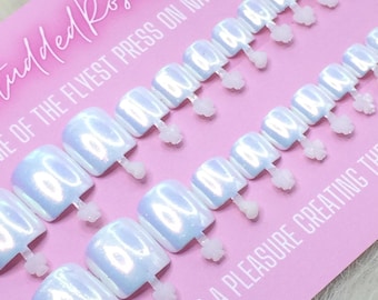 May include: A set of square-shaped press-on nails with a pearlescent, iridescent finish attached to a pink display card. The card features the text StuddedRoseNails, THE OF THE FLYEST PRESS ON NAILS AROUND!, and -IT WAS A PLEASURE CREATING TH.