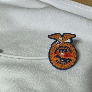 May include: A blue and orange plastic pin with the words "Agricultural FFA Education" and an eagle design.
