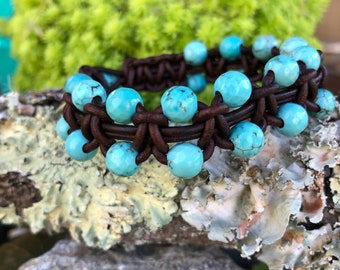 May include: A brown leather bracelet with turquoise beads. The bracelet is woven with a knot pattern.