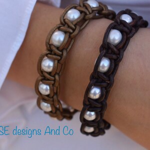 May include: Two leather bracelets with white pearl accents. The bracelets are woven in a braided pattern. One bracelet is brown and the other is gold.