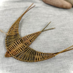 Könnte beinhalten: Ein handgefertigter, dekorativer Vogel aus geflochtenen braunen Zweigen. Der Vogel hat ausgebreitete Flügel und ein schlichtes, rustikales Design. Ein dünner, naturfarbener Faden ist zum Aufhängen befestigt. Ein charmantes Wohnaccessoire.