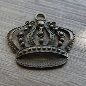 May include: A bronze crown charm with a decorative design. The crown has a loop at the top for hanging.