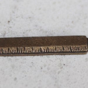 May include: A small, antique gold-toned metal ruler charm with a loop for attaching to a necklace or bracelet.