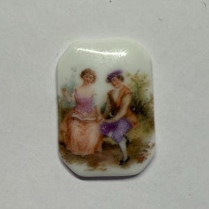 Peut inclure: Plaque rectangulaire en porcelaine avec une scène peinte de deux personnages en costume d'époque. Les personnages sont représentés dans des tons de rose, de violet et de marron sur un fond de verdure. La plaque a une finition brillante.