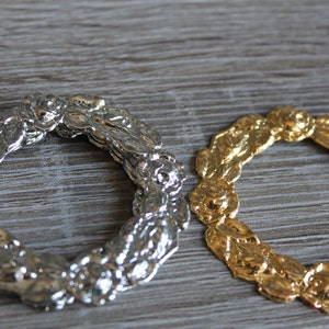 Pode incluir: Duas coroas decorativas, uma prateada e outra dourada, com um design floral. As coroas são de metal e têm forma circular.
