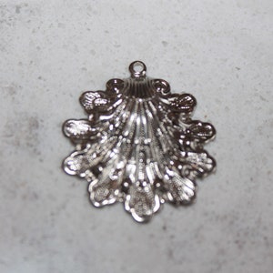 Könnte beinhalten: Silberner Metallanhänger in Form einer Muschel mit einem detaillierten Design.