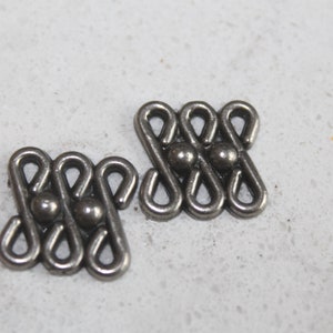 Könnte beinhalten: Zwei silberne Metall-Dekorationsstücke mit geometrischem Design. Jedes Stück hat drei Kreise in der Mitte.