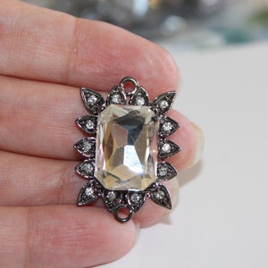 Puede incluir: Un gran cristal transparente facetado est&aacute; engastado en un marco de metal plateado con un dise&ntilde;o floral decorativo. El marco tiene peque&ntilde;os diamantes de imitaci&oacute;n transparentes alrededor del borde.