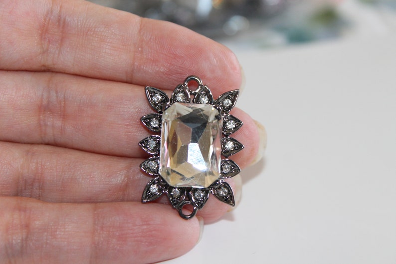 Puede incluir: Un gran cristal transparente facetado est&aacute; engastado en un marco de metal plateado con un dise&ntilde;o floral decorativo. El marco tiene peque&ntilde;os diamantes de imitaci&oacute;n transparentes alrededor del borde.