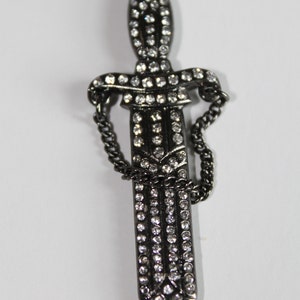 May include: A black metal dagger pendant with a chain and clear rhinestones.