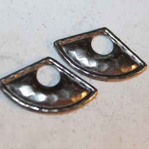 Könnte beinhalten: Zwei silberfarbene, fächerförmige Metallkomponenten mit einem kreisförmigen Loch in der Mitte. Die Teile haben eine reflektierende Oberfläche und liegen auf einer hellen, gesprenkelten Oberfläche.