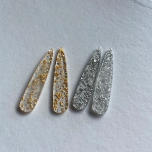 Op de afbeelding: Vier doorzichtige, traanvormige oorbellen van plastic met ingebedde gouden en zilveren glitter.