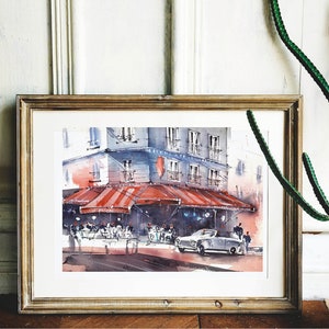 Puede incluir: Una pintura de acuarela en un marco dorado representa una escena de calle parisina con un caf&eacute; bajo un toldo a rayas rojas y blancas. La gente est&aacute; sentada en mesas fuera del caf&eacute;, y un coche est&aacute; aparcado en la calle. La pintura est&aacute; sobre un fondo blanco.