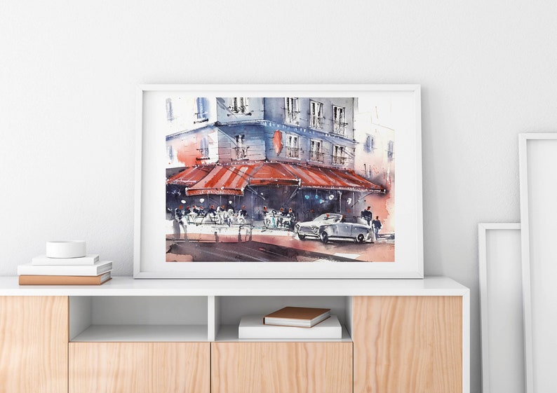 Puede incluir: Una pintura de acuarela de un caf&eacute; parisino con una marquesina roja a rayas, mesas y sillas, y un coche antiguo estacionado en frente. El edificio est&aacute; pintado en tonos de azul y gris, y el cielo es de un azul suave.