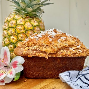 May include: A loaf of banana bread topped with shredded coconut and a pineapple on a wooden surface.