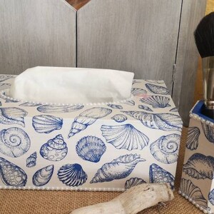 Peut inclure: Un couvre-boîte à mouchoirs blanc avec un motif de coquillages bleu et blanc. Un porte-crayons assorti avec un motif de coquillages bleu et blanc se trouve à côté du boîte à mouchoirs.