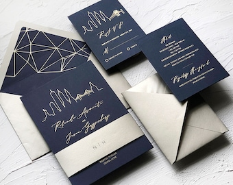 Puede incluir: Conjunto de invitaciones de boda azul marino con detalles en dorado. La invitación presenta una silueta de horizonte y los nombres de la pareja. La tarjeta RSVP tiene un diseño de ciudad en dorado. La tarjeta de detalles tiene una fuente de escritura dorada.