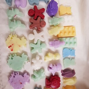 May include: Assortment of colorful wax melts shaped like various objects, including a guitar, gingerbread man, a rocking horse, a cat, a penguin, and a Lego brick.