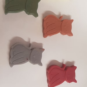 Op de afbeelding: Zes katvormige wax melts in verschillende kleuren: geel, groen, oranje, grijs en rood. De melts zijn gerangschikt op een wit oppervlak. Ideaal voor huisgeur.