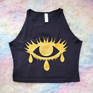 May include: A black tank top with a gold eye graphic. The eye is dripping with gold tears.