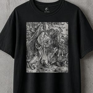 May include: A black short-sleeve t-shirt featuring a detailed monochromatic graphic print on the chest. The artwork depicts a classical scene of an angel and a demonic figure in a landscape, with the initials AD visible in the lower left corner.