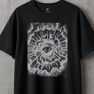 May include: Black t-shirt with a graphic of an eye within a sunburst design. The eye is centered within a cloud-like frame. The t-shirt is hanging on a metal hanger against a gray concrete wall.