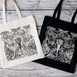 May include: Two tote bags with black and white illustrations of a circular design with text in Latin. The design features a circle with a star inside and is surrounded by eight smaller circles with text in Latin. The tote bags are made of canvas and have black handles. One tote bag is white and the other is black.