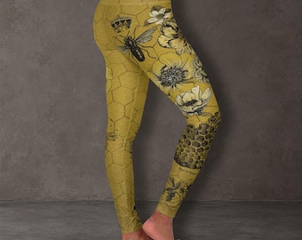 May include: High-waisted leggings in a mustard yellow hue featuring a repeating hexagonal honeycomb pattern. The design includes black and white illustrations of a bee, a crown, and various floral motifs across the fabric surface.