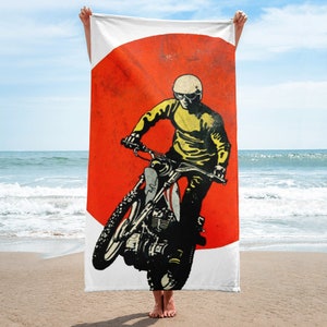 Puede incluir: Una toalla de playa con una ilustración vintage de una persona conduciendo una motocicleta frente a un sol rojo.