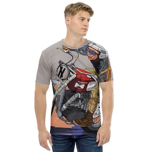 May include: A light gray t-shirt featuring a colorful illustration of a vintage motorcycle and rider. The motorcycle is red with the text "Husqvarna Champion". The rider wears goggles and a helmet. The number "5" is visible on the motorcycle.